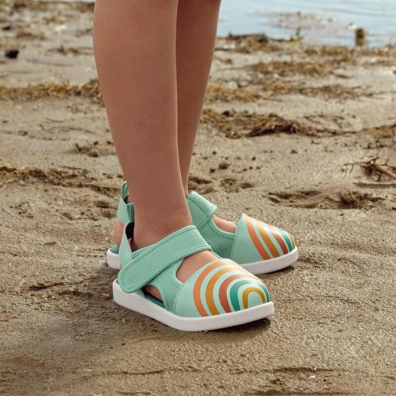 Child standing on beach wearing Rainbow sandals