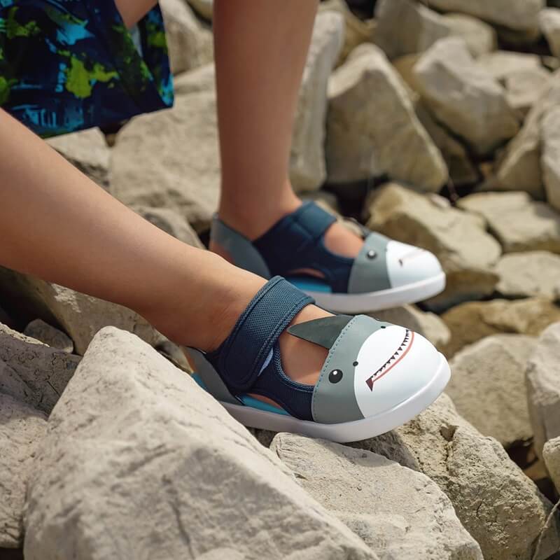 Child wearing Shark sandals on rocky surface